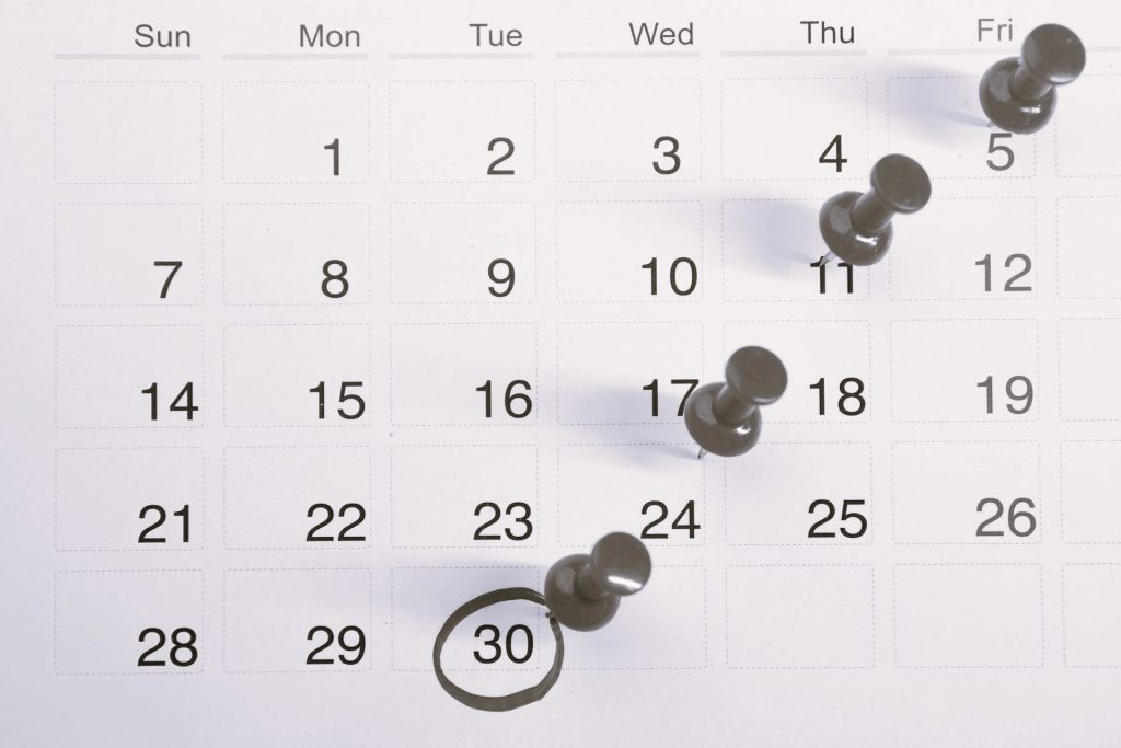 A close-up of a calendar with multiple dates pinned with thumbtacks, symbolising scheduling, rostering, and planning challenges in workforce management.